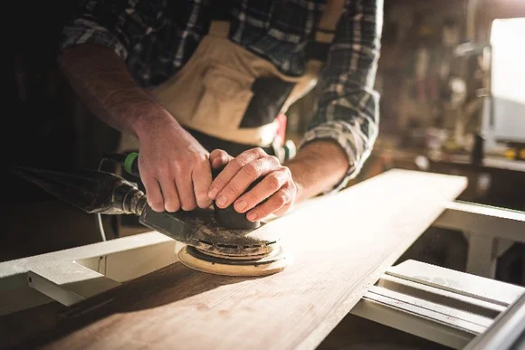 Person schleift Holzbrett mit Schleifmaschine